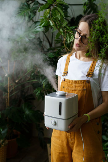 Young gardener girl use humidifier for humidity indoors during heating season caring for houseplants