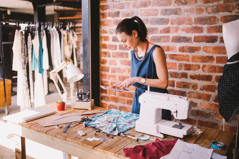 Adults Only Candid Casual Clothing Creativity Design Professional Desk Digital Tablet Entrepreneur Expertise Fashion Fashion Designer Indoors Lifestyles Occupation Office One Person One Woman Only Only Women Real People Sewing Machine Skill Small Business Standing Working Young Adult Modern Workplace Culture
