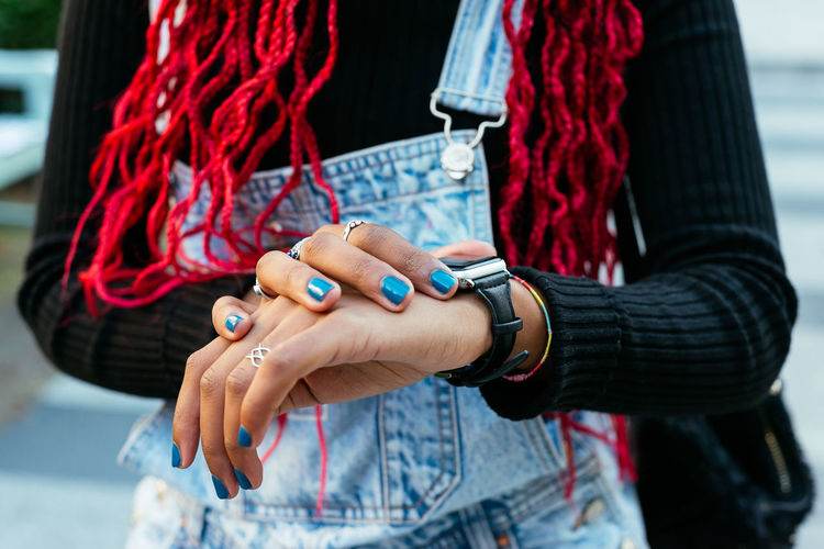 From above of crop anonymous black female wearing rings on manicured fingers with blue nail polish touching wristwatch