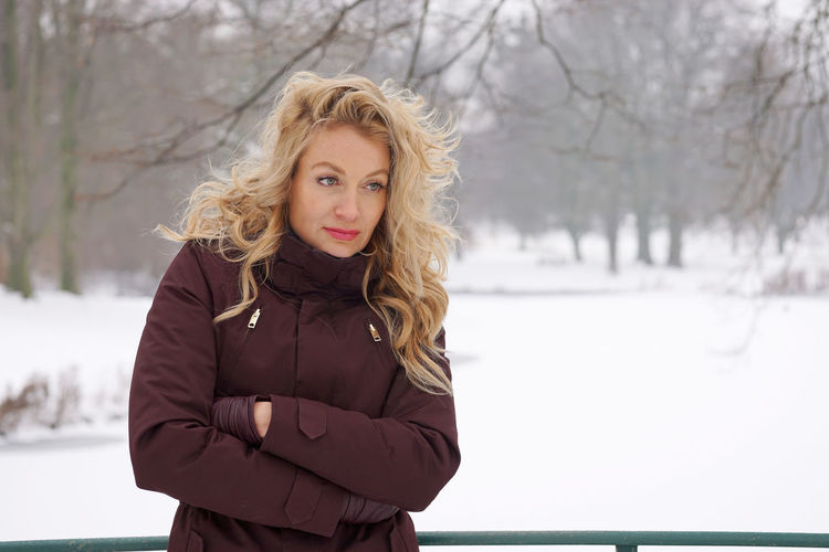 Thoughtful woman with arms crossed standing on snow covered field