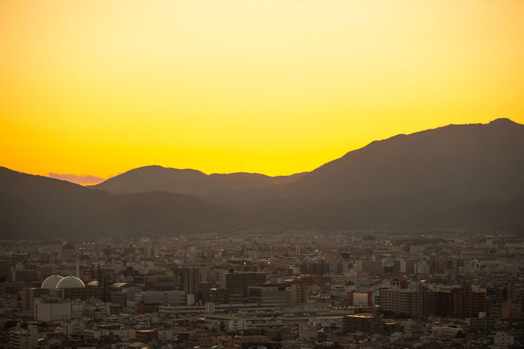 Aerial view of townscape by mountains against orange sky
