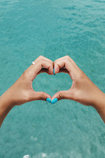 Close-up of hands holding heart shape against blue water