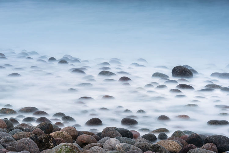 Long exposure of surf breaking on large boulders on the shore