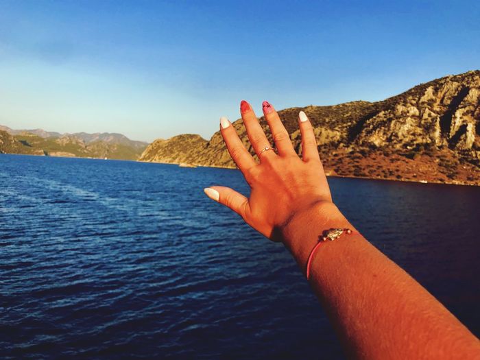Cropped hand of woman gesturing at lakeshore against mountains