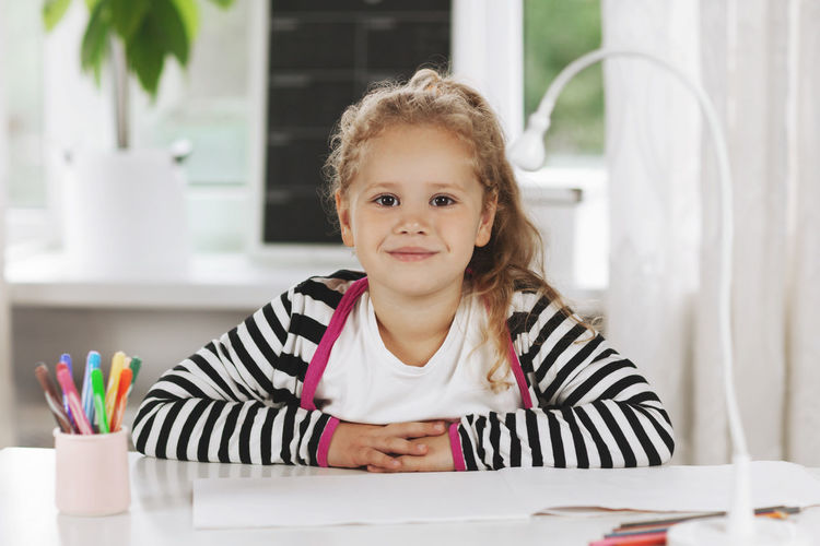 Portrait of a charming little girl sitting at a table. the girl is sitting at the table