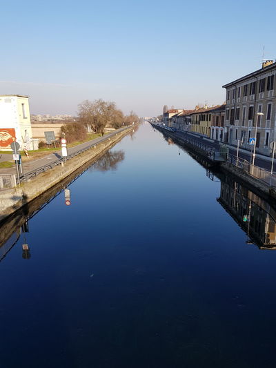 Reflection of buildings in canal against clear blue sky