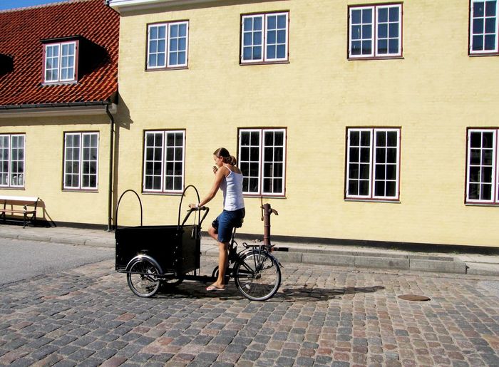Woman riding cargo bike on street against buildings during sunny day