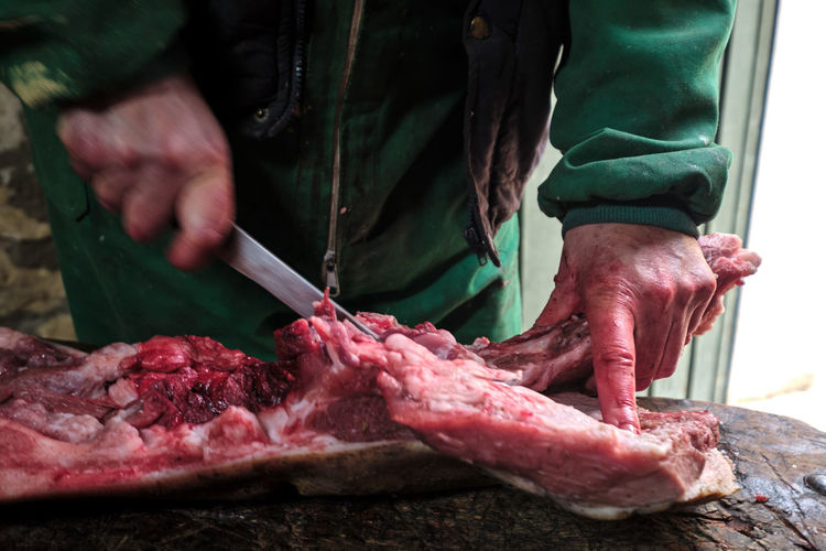 Midsection of butcher cutting meat on table