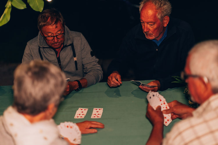Friends senior people playing cards outdoor on a spring summer night