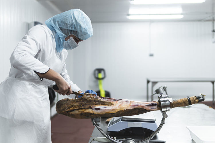 Woman employee cutting ham leg in factory
