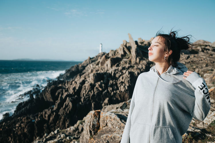 Side view of young woman standing at beach against sky