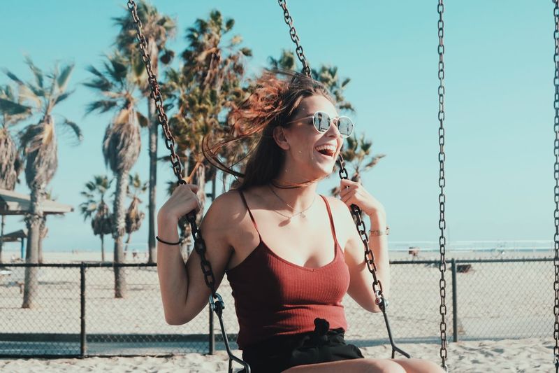 Young woman in sunglasses swinging against clear sky
