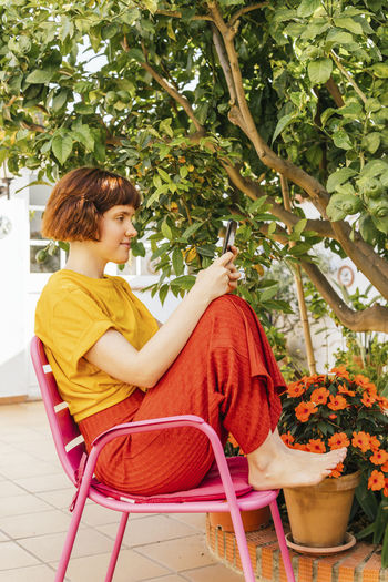 Woman using smart phone while sitting on chair in home garden