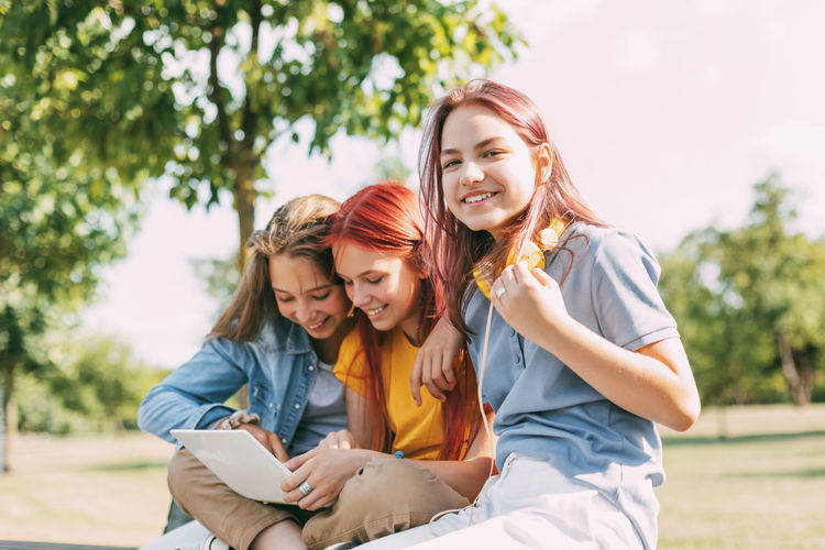 Attractive teenage girls are sitting on a park bench, discussing and smiling. 
