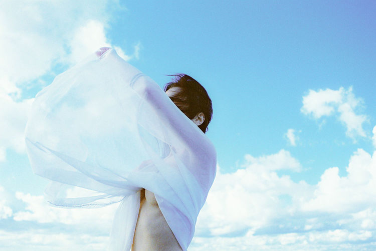 Seductive woman wearing white dress standing against blue sky