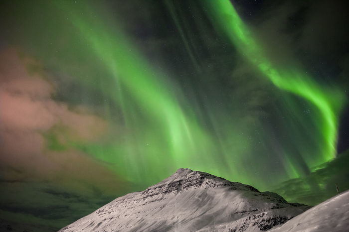 Low angle view of aurora borealis over snowcapped mountain at night