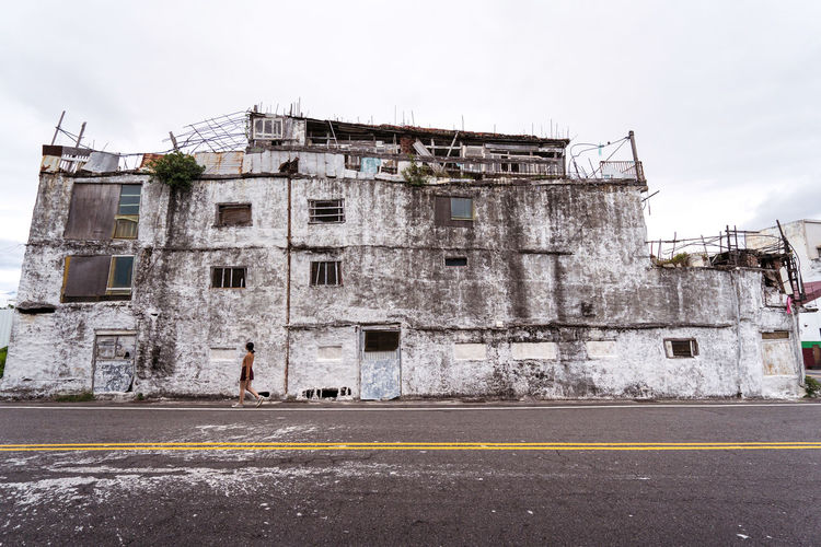 Unrecognizable female walking along pavement with shabby abandoned building located against gray sky on east coast