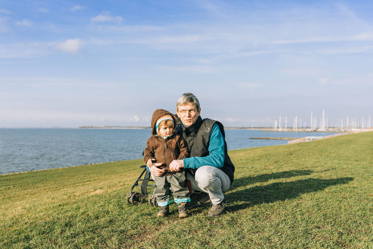 Portrait of mature man with granddaughter at beach by sea against sky