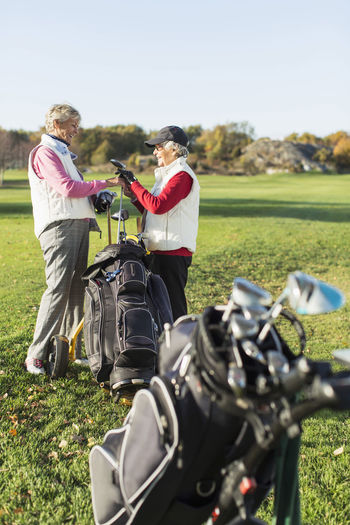 Side view of senior female friends choosing golf club on golf course