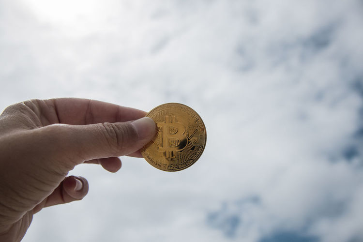Close-up of hand holding coin against cloudy sky