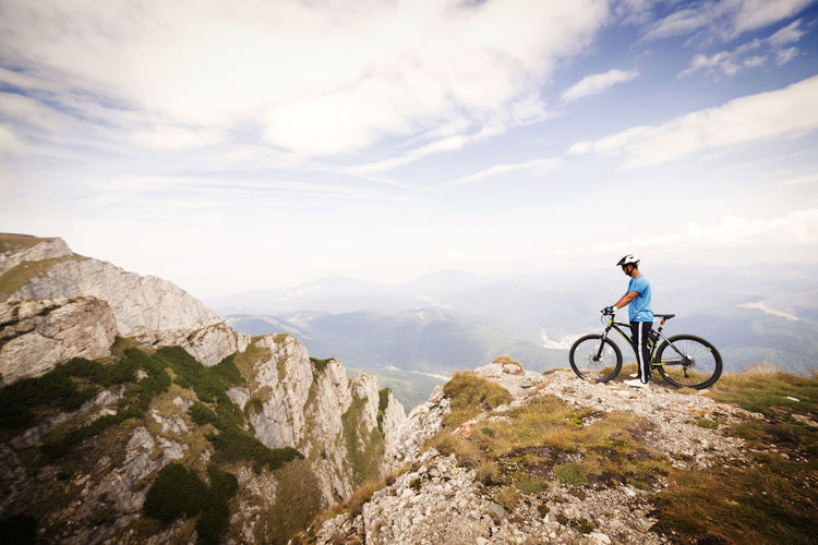 Side view of mountain biker with bicycle against cloudy sky