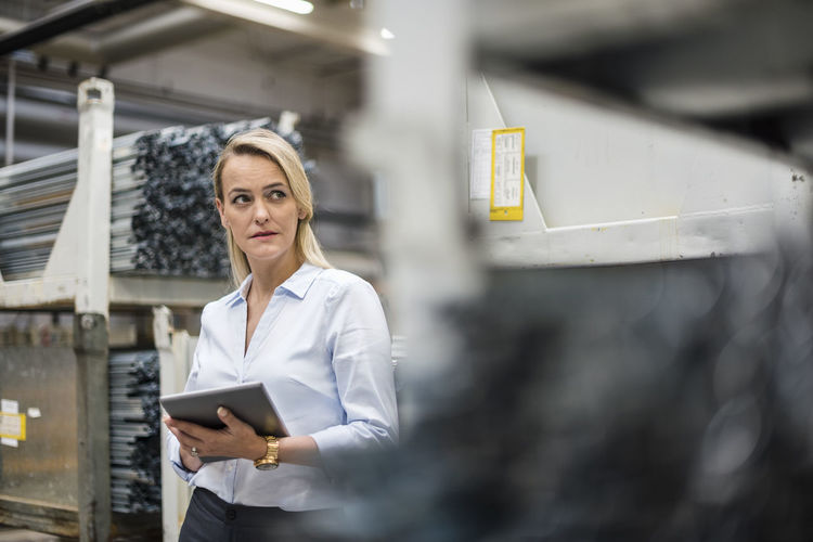 Blond woman holding tablet in high rack warehouse
