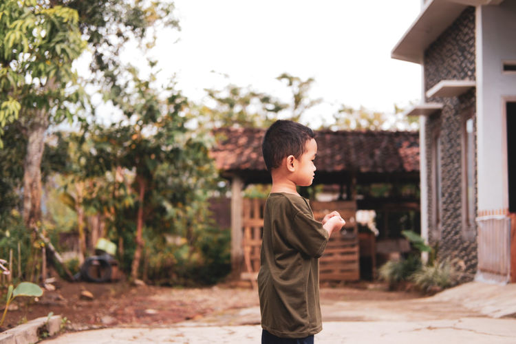 Side view of boy standing against trees