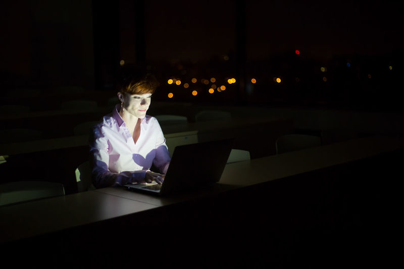 Woman using phone while sitting on table at night