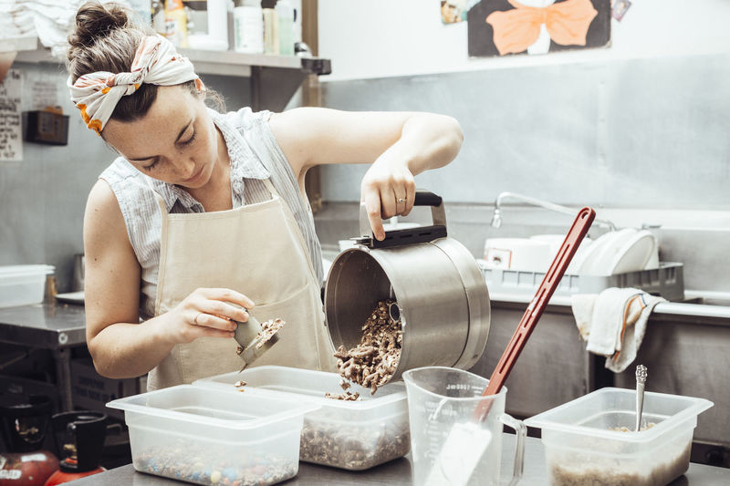 Woman pouring grinded ingredients in container while making ice cream at commercial kitchen
