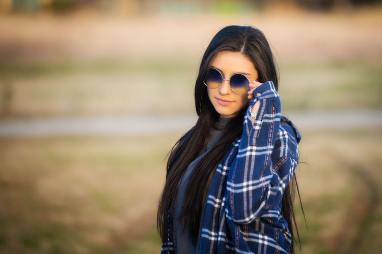 Portrait of fashionable young woman wearing sunglasses while standing on land