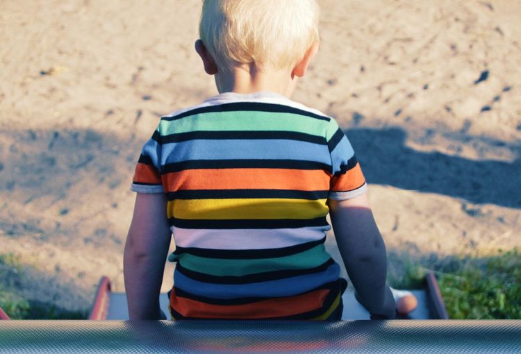 Rear view of boy sitting on slide at playground