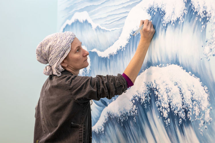 Mature woman artist draws a mural on a marine theme, close up