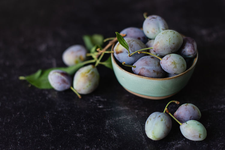 Close up image of a bowl of fresh plums against a black background.