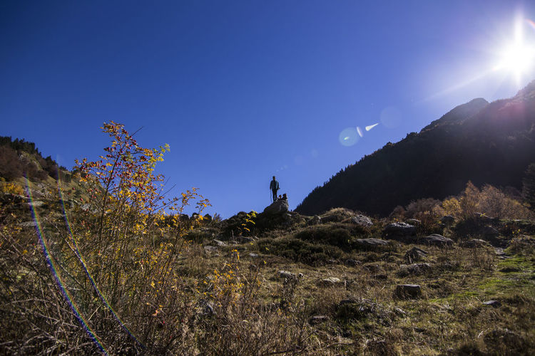 Low angle view of male hiker standing on cliff against clear blue sky