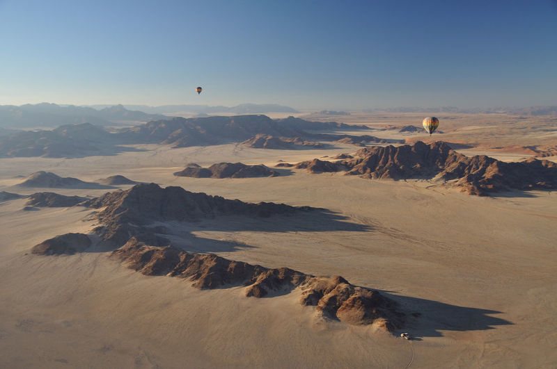 Scenic view of namib desert against sky, with hot air balloons