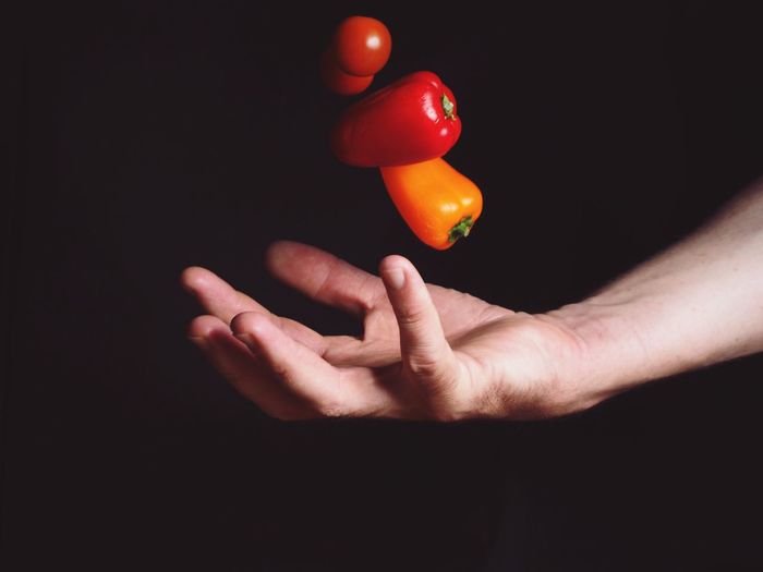 Close-up of hand holding tomato over black background