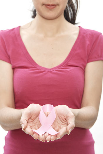 Midsection of woman holding breast cancer awareness ribbon against white background