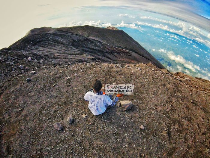 High angle view of man sitting with text on rock against sky