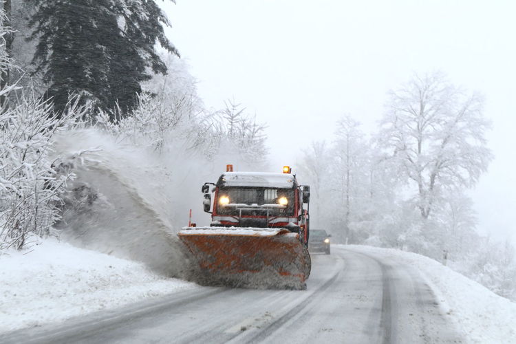 Snow plough on road by trees during winter