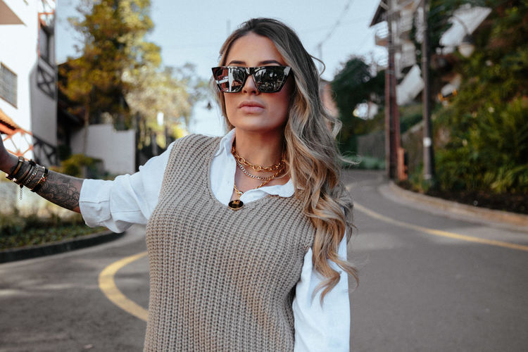 Portrait of young woman wearing sunglasses standing on road in city