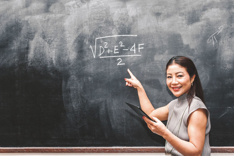 Portrait of teacher pointing at formula on blackboard in classroom