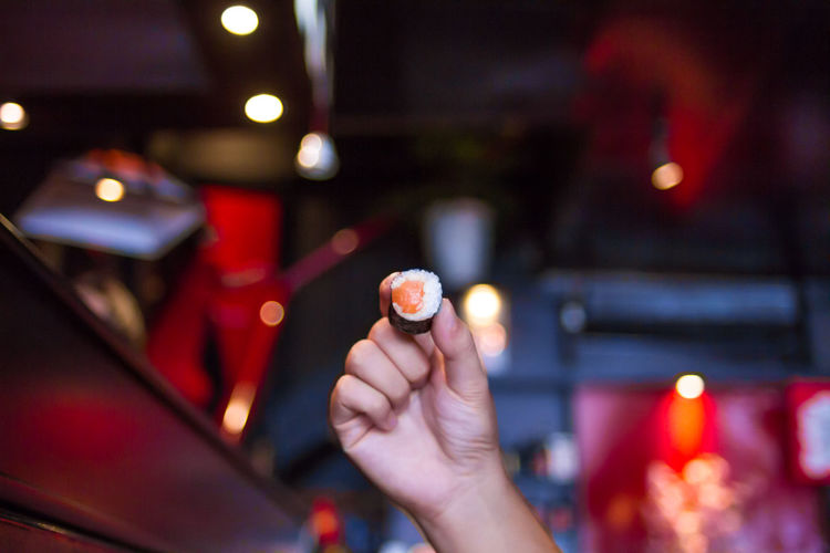Cropped image of hand holding sushi at night