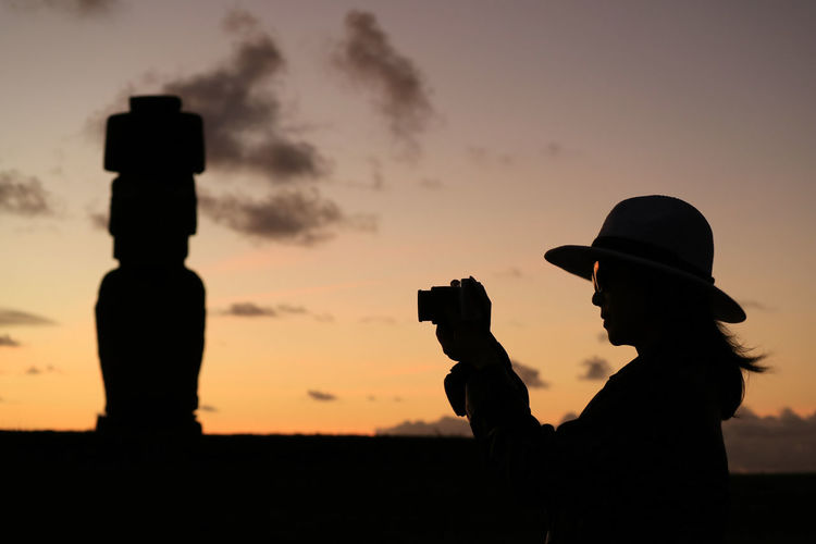 Side view of silhouette woman photographing with camera against sky during sunset