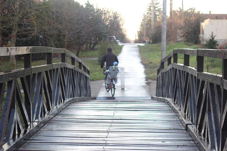 Rear view of man riding bicycle on bridge