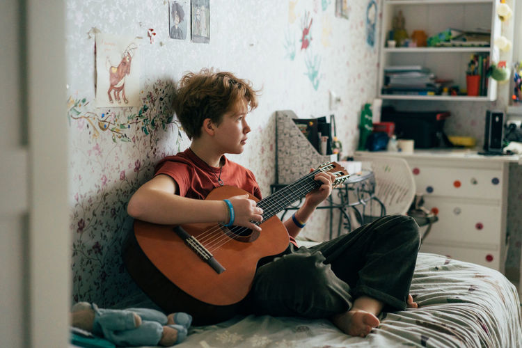Romantic teenage redhead girl learning to play the guitar while sitting in the room.