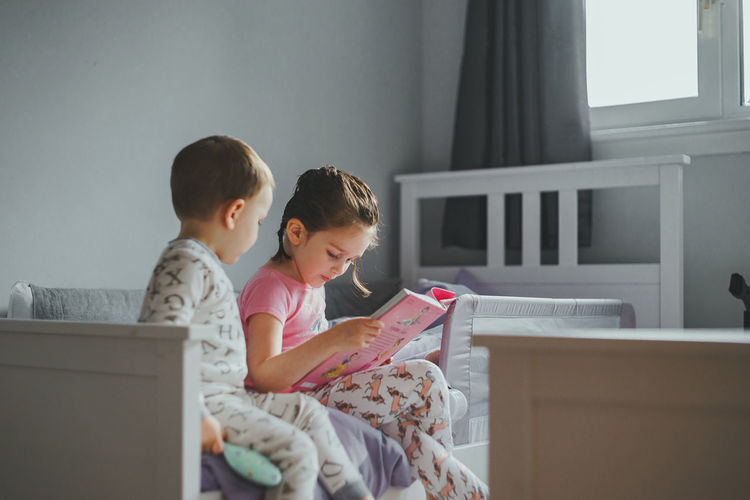 Young girl reading a story book to her brother before bedtime
