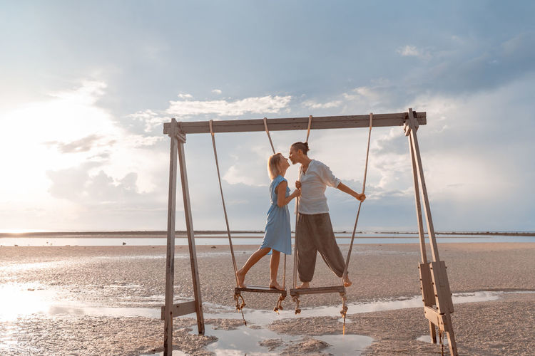 Rear view of man and women standing on swing at beach