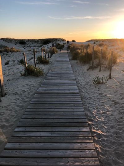 Boardwalk leading towards beach against sky during sunset