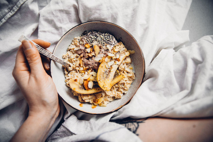 Close-up of hand eating granola in bowl on bed