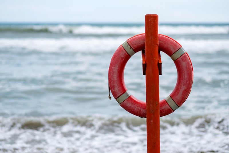 Close-up of red life belt hanging on pole against sea